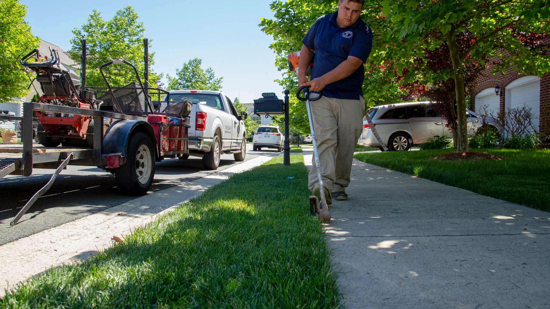 Professional edging a lawn by the sidewalk with a company trialer in the background.
