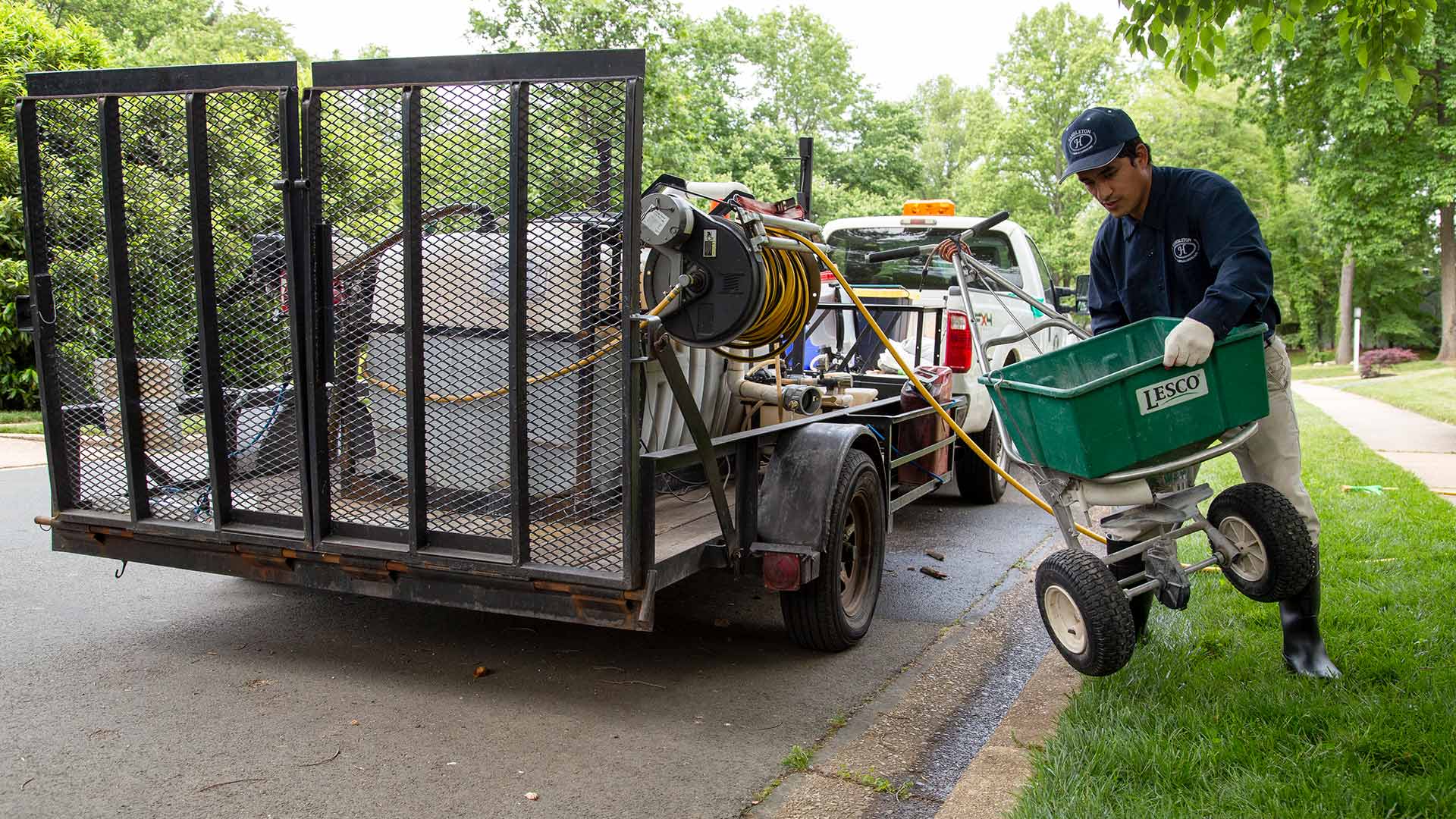 A man setting up a fertilizer spreader by a work trailer in the street in Fairfax, VA.