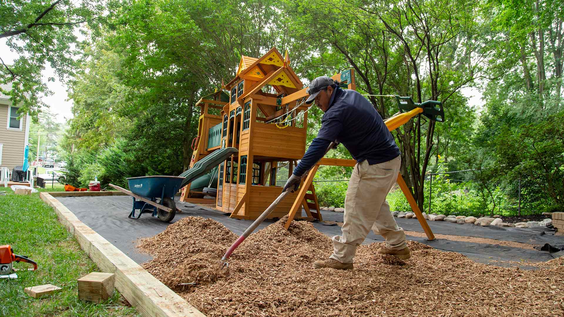 A worker is spreading new mulch around the base of a playground in a backyard in Falls Church, VA.