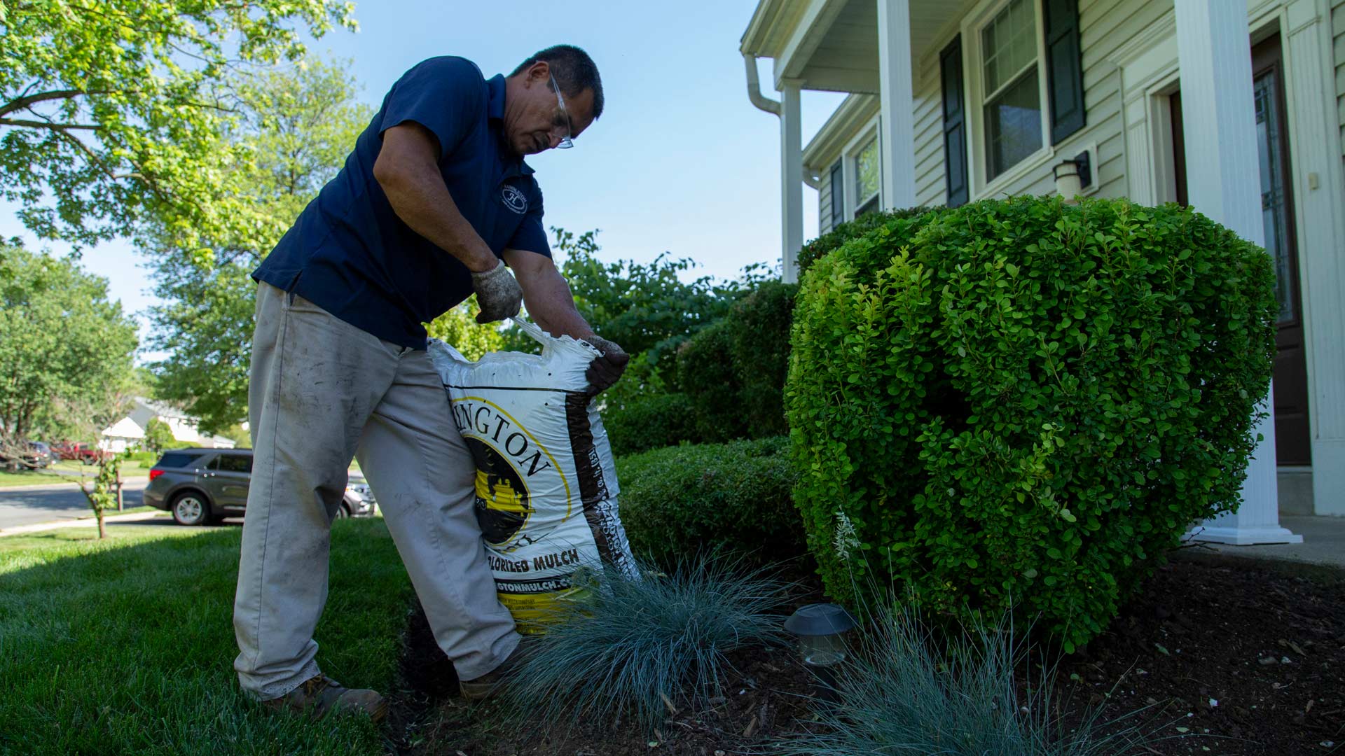 A man opening a bag of mulch to spread it onto a landscape bed.