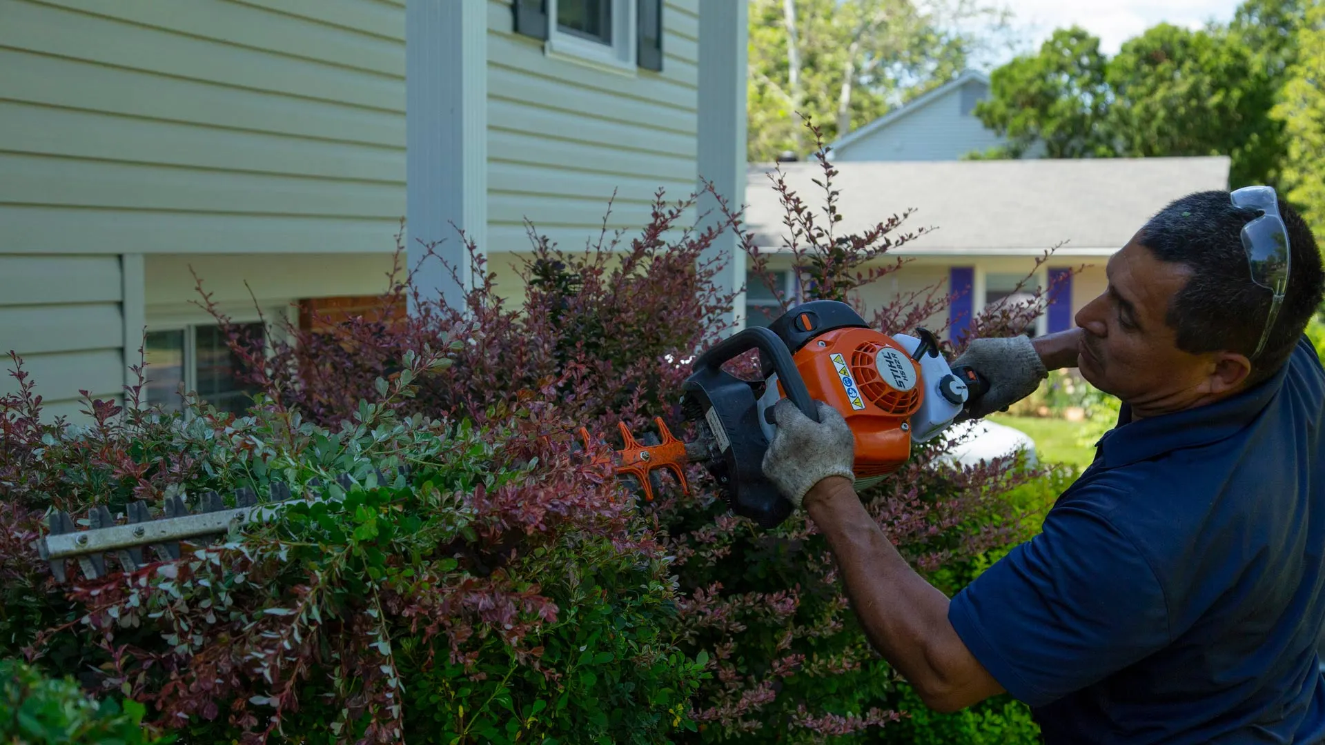 Man raking a landscape bed, removing leaves, weeds, and debris.