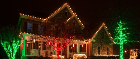 A house with holiday lighting along the windows, doorway, roofline, shrubs and small trees.