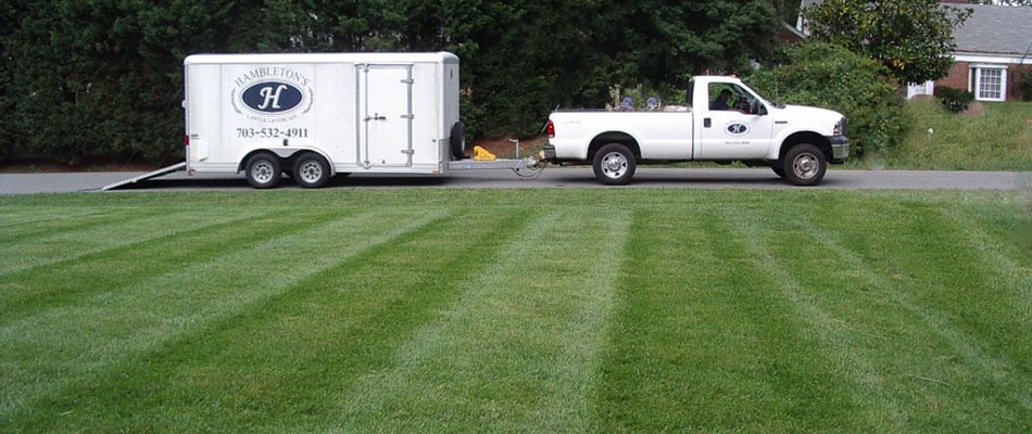 A Hambleton Lawn & Landscape company truck and trailer at the edge of a lawn they just finished mowing.
